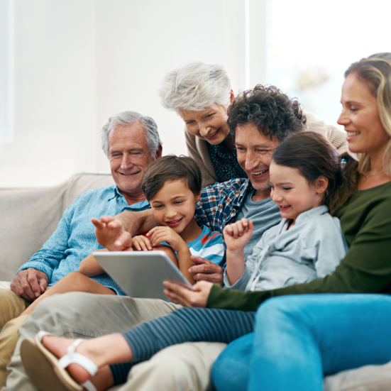En familie med forældre, bedsteforældre og børn læser sammen i en sofa