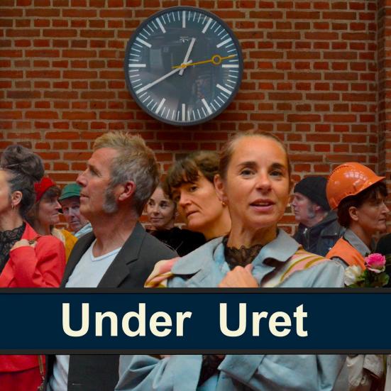 En masse mennesker på en togstation. De står under et stort ur. 