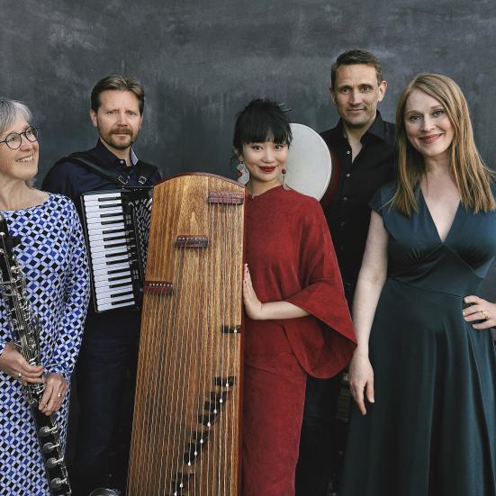 Fem velklædte musikere ved siden af hinanden, i midten står en kvinde med et kinesisk musikinstrument, en guzheng. 