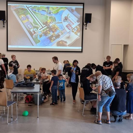 En gruppe mennesker i en sal med LEGO-robotter på borde.