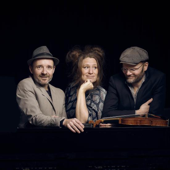 Tre musikere med en violin på en mørk baggrund.