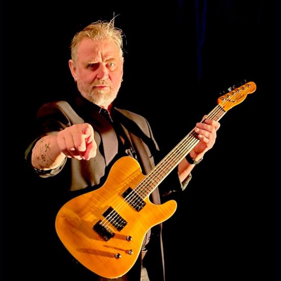 En mand står med en elektrisk guitar og peger ud mod beskueren. 