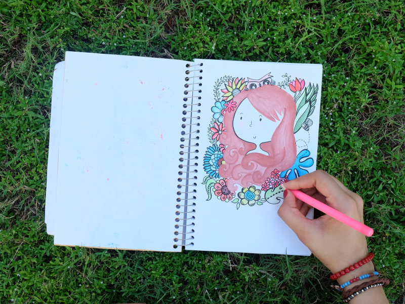 Et foto af en opslået notesbog, hvor man ser en hånd, der tegner et pigeansigt.