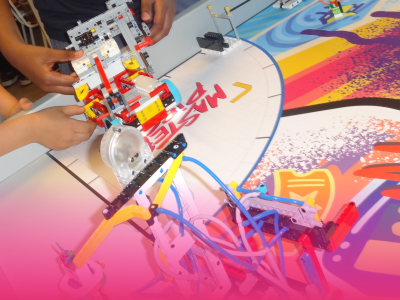 To sæt hænder er ved at bygge en robot af LEGO, som står på et bord. 