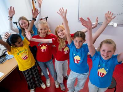 Børn i blå t-shirts med popcornbægre på ser glade ud og rækker hænderne i vejret 