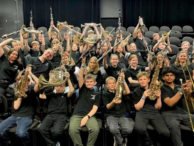 En stor gruppe sidder med deres blæseinstrumenter i en koncertsal