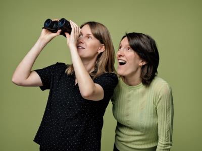 To kvinder står og kigger ud, den ene med en kigger i hånden, som hun holder op foran sine øjne. 