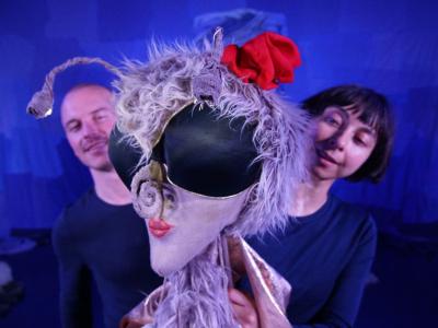 To skuespillere i en teaterkulisse står bag en dukke. 