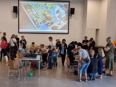 En gruppe mennesker i en sal med LEGO-robotter på borde.
