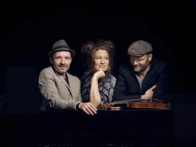 Tre musikere med en violin på en mørk baggrund.