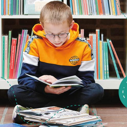 En dreng sidder på gulvet og læser i en bog på et bibliotek.