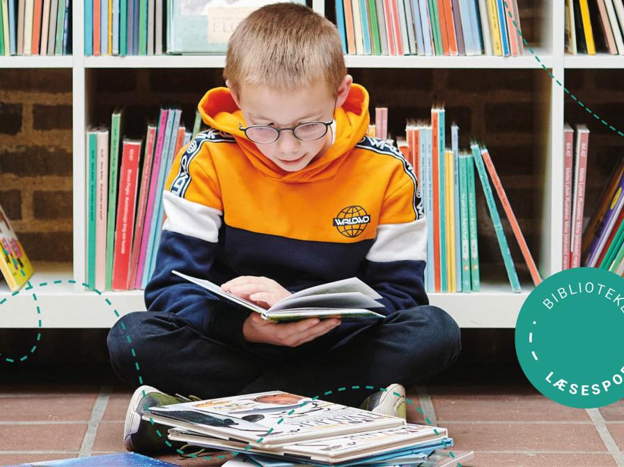 En dreng sidder på gulvet og læser i en bog på et bibliotek.