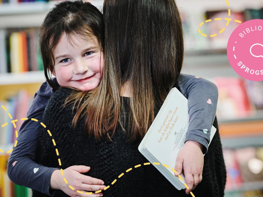 En pige bæres af en kvinde, der står med ryggen til. Pigen smiler og holder en bog i hånden.