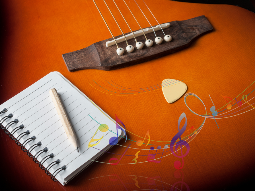 En guitar hvorpå der ligger en linjeret blok og en blyant. På guitaren er der også indsat noder i forskellige farver.