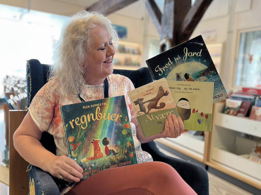 Foto af bibliotekar, der sidder med børnebøger i en stol i børnebiblioteket