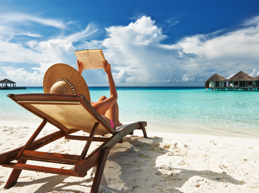 Kvinde med bog i liggestol på strand