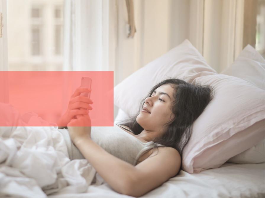 Ung kvinde ligger i seng og læser på sin telefon